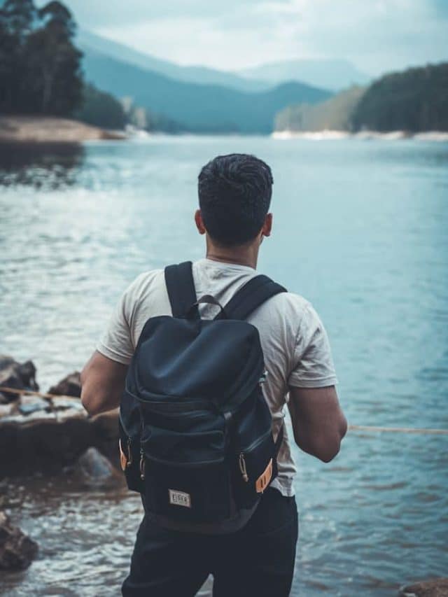 man in gray shirt and black backpack standing on rocky shore during daytime